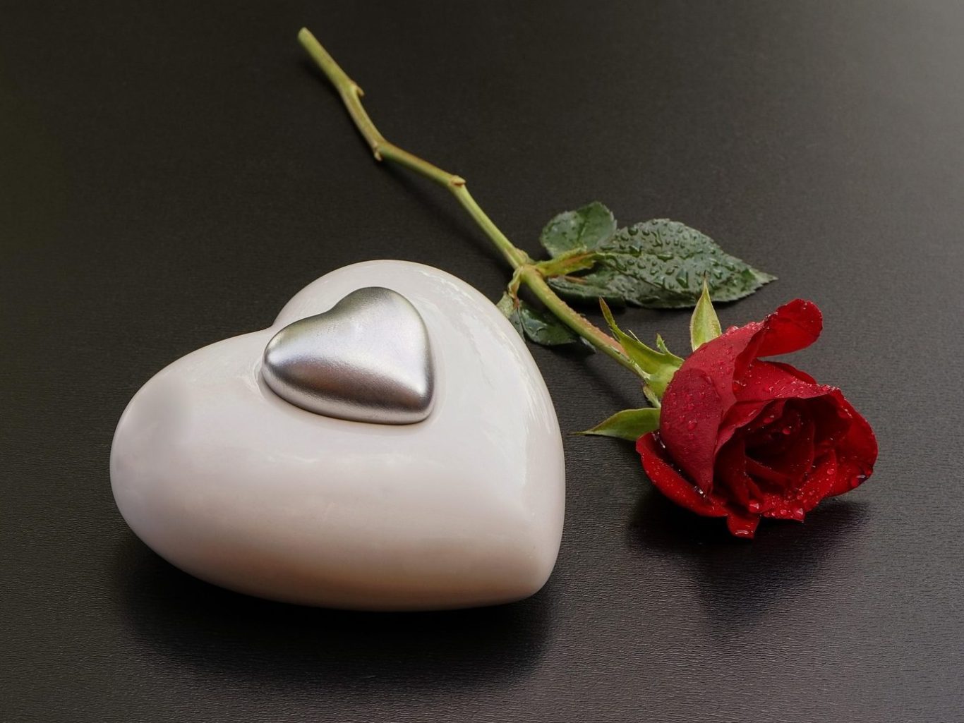 Eine herzförmige Steinskulptur mit einem metallischen Herz und einer roten Rose.