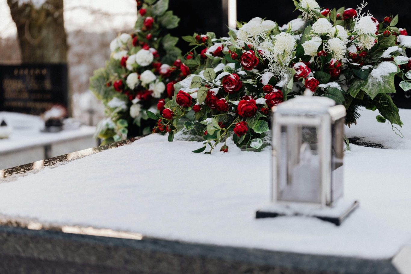 Grabstein mit einer Laterne und roten sowie weißen Rosen im Schnee.